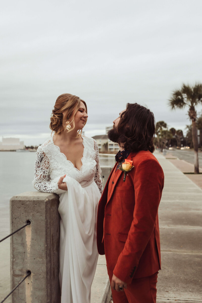 newlyweds smile at each other wearing wedding dress and vintage red retro suit - in panama city cove downtown overlooking Bay