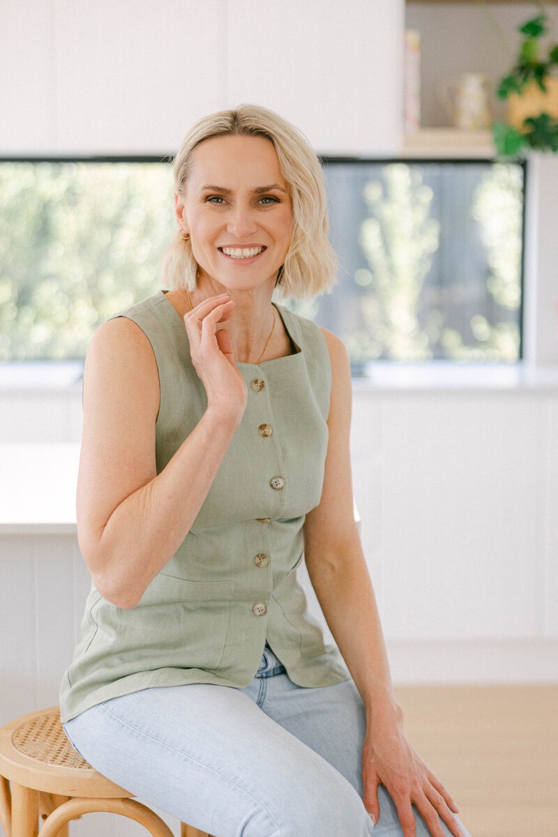 Zelda Green, entrepreneur and money and mindset educator, smiling at camera while working on her laptop on her business resources in a beautiful home