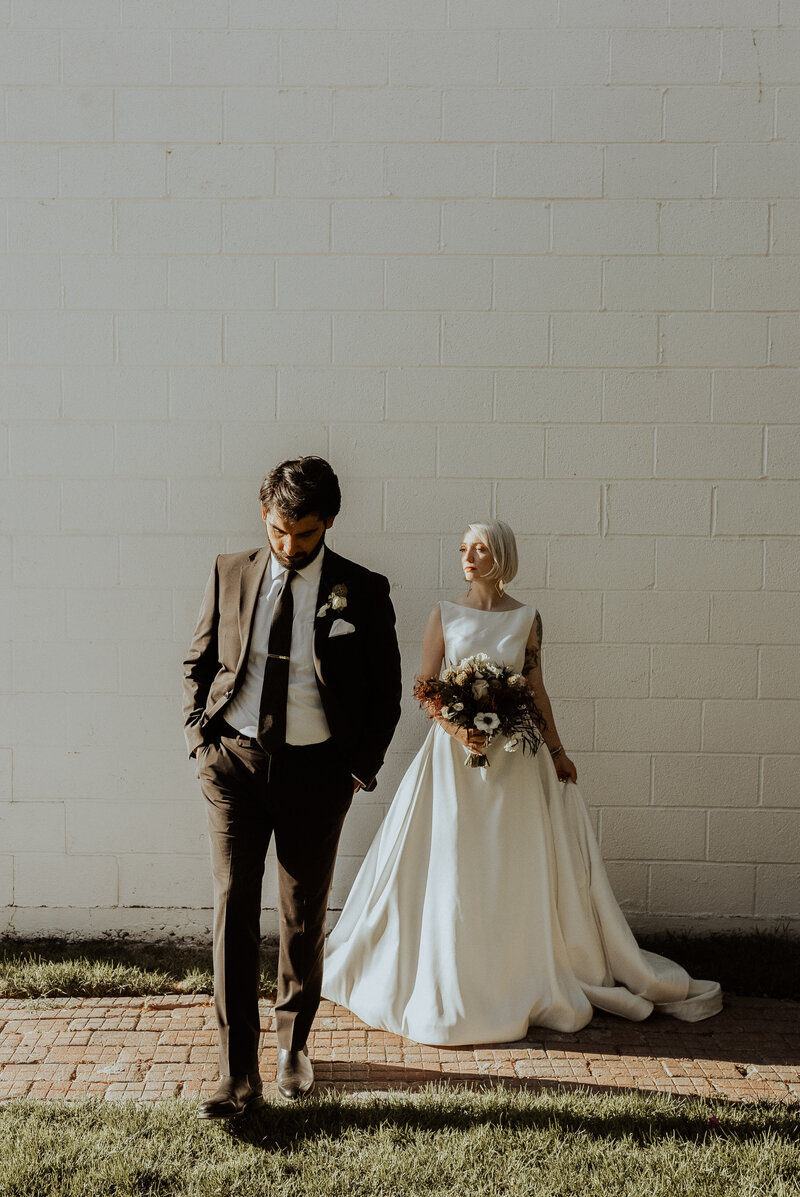 Editorial quirky magazine worthy wedding portrait of a modern couple in minimalist styling, captured in dramatic natural light against a neutral wall during a luxury Fresno CA wedding.