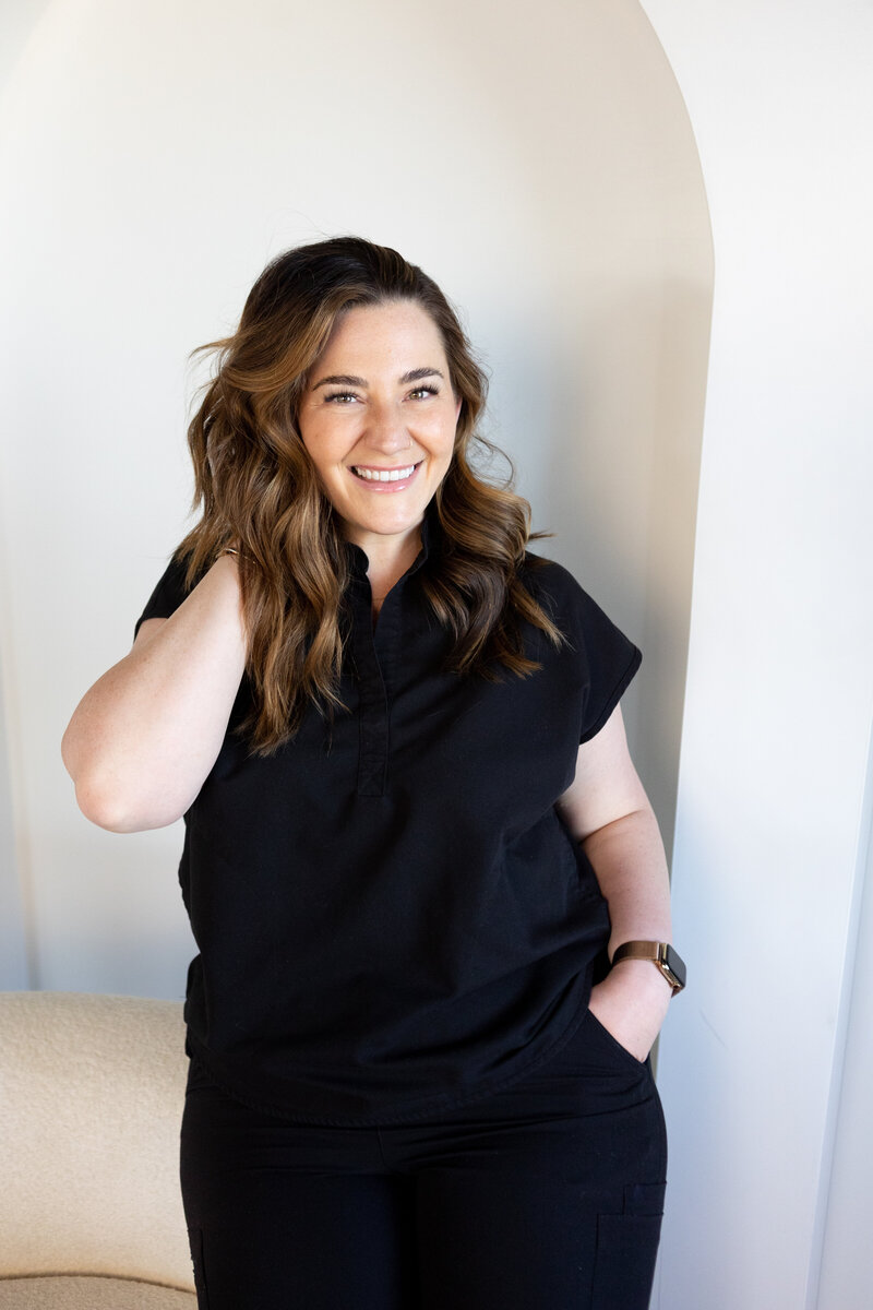 Allie Osugi wearing black scrubs with a hand in her pocket and a hand in her hair