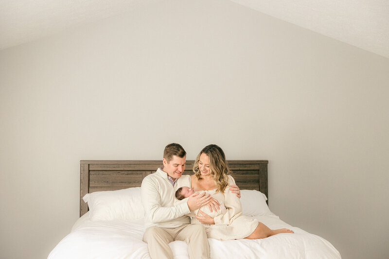 New parents sit on their bed and hold their baby during their in home newborn session, Indianapolis photographer