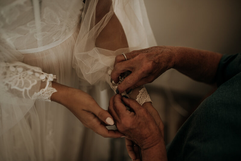grandmother buttoning brides sleeves on her wedding dress