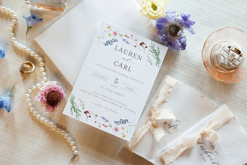 Flat lay details of wedding invitation, vow books, and pearls 
