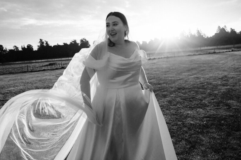 black and white photo of bride swirling veil in front of sunset at bangor farm