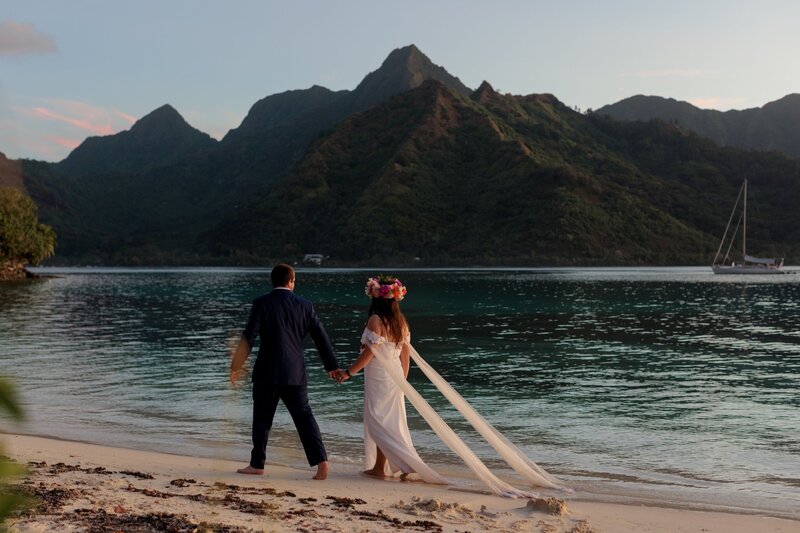 bride and groom walk along the beach on Moorea with the island of Tahiti in the background