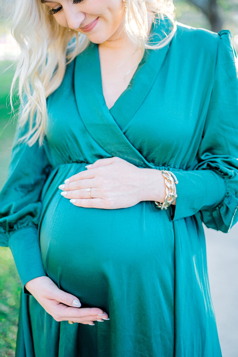 Close up image of a pregnant woman in a green dress with her hands around her stomach