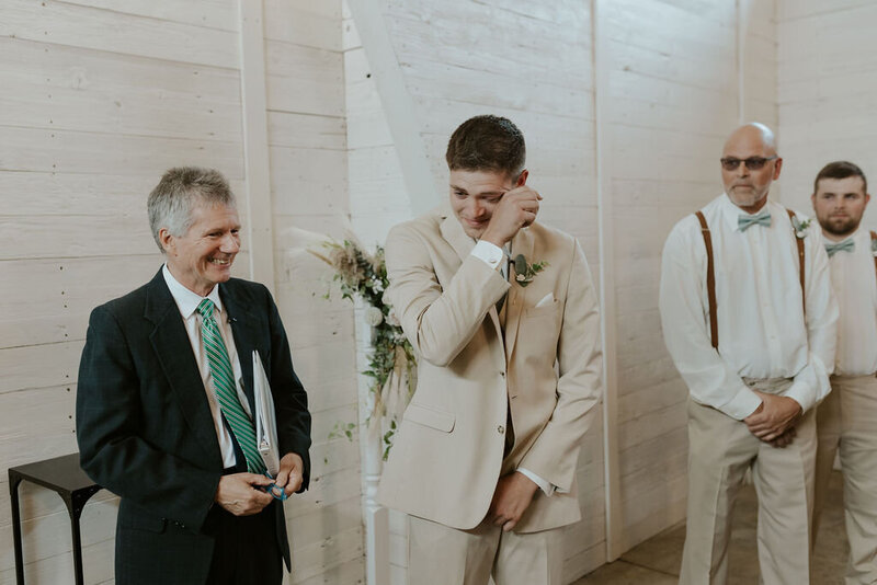 Groom in tan suit standing at the alter brushing away tears