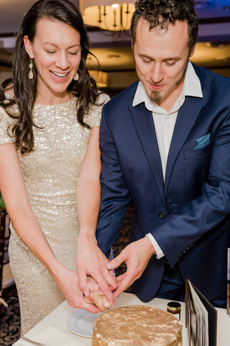 Well dressed couple cutting a gold wedding cake.