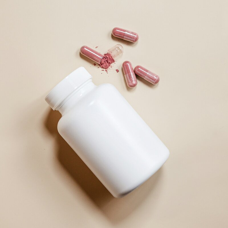 White supplement bottle with opened herbal capsules on a neutral background, representing natural health support and personalized supplementation