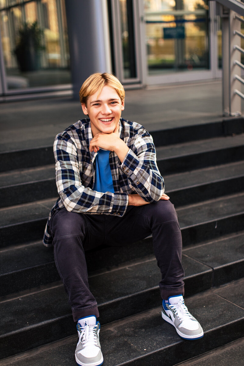 A blonde laughing student sits on the stairs of a high-rise building downtown Pittsburgh.