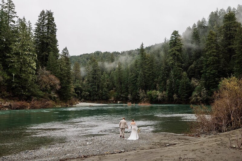 A bride and groom walk along the Smith River in Redwood State Park.