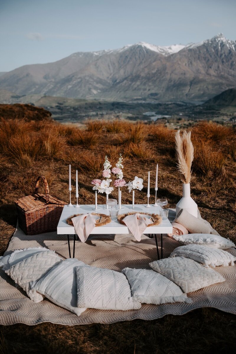 A couple eloping in the mountains of Queenstown cutting their cake in a styled picnic