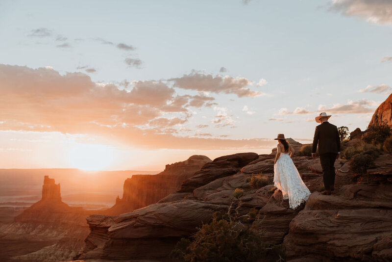 bride and groom standing before a large red rock formation in the desert