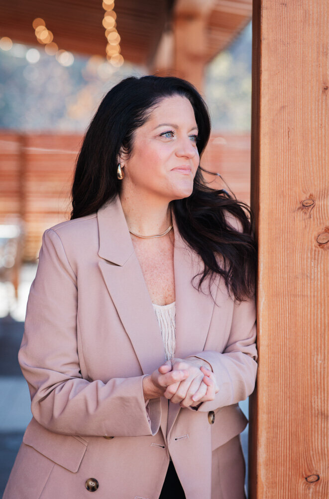 Alison Seponara in a pink blazer leaning against a cedar post