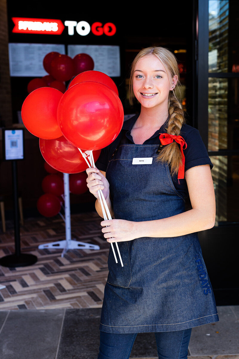 A smiling girl holding red balloons at the opening of TGI Fridays in Tuggerah on the NSW Central Coast. A Corporate Launch Event photographed by Underatreehouse Photography.