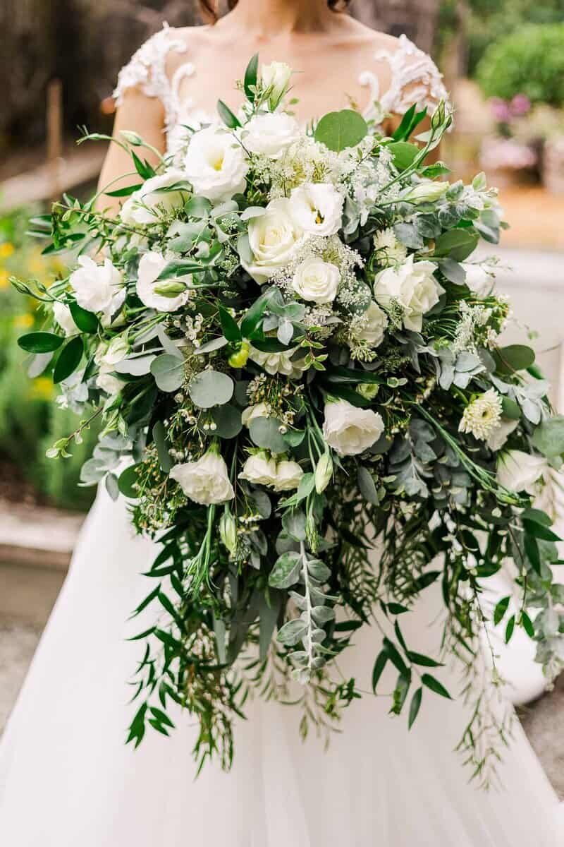 Bride holding massive bouquet of greenery and white flowers that go down to her mid-thighs