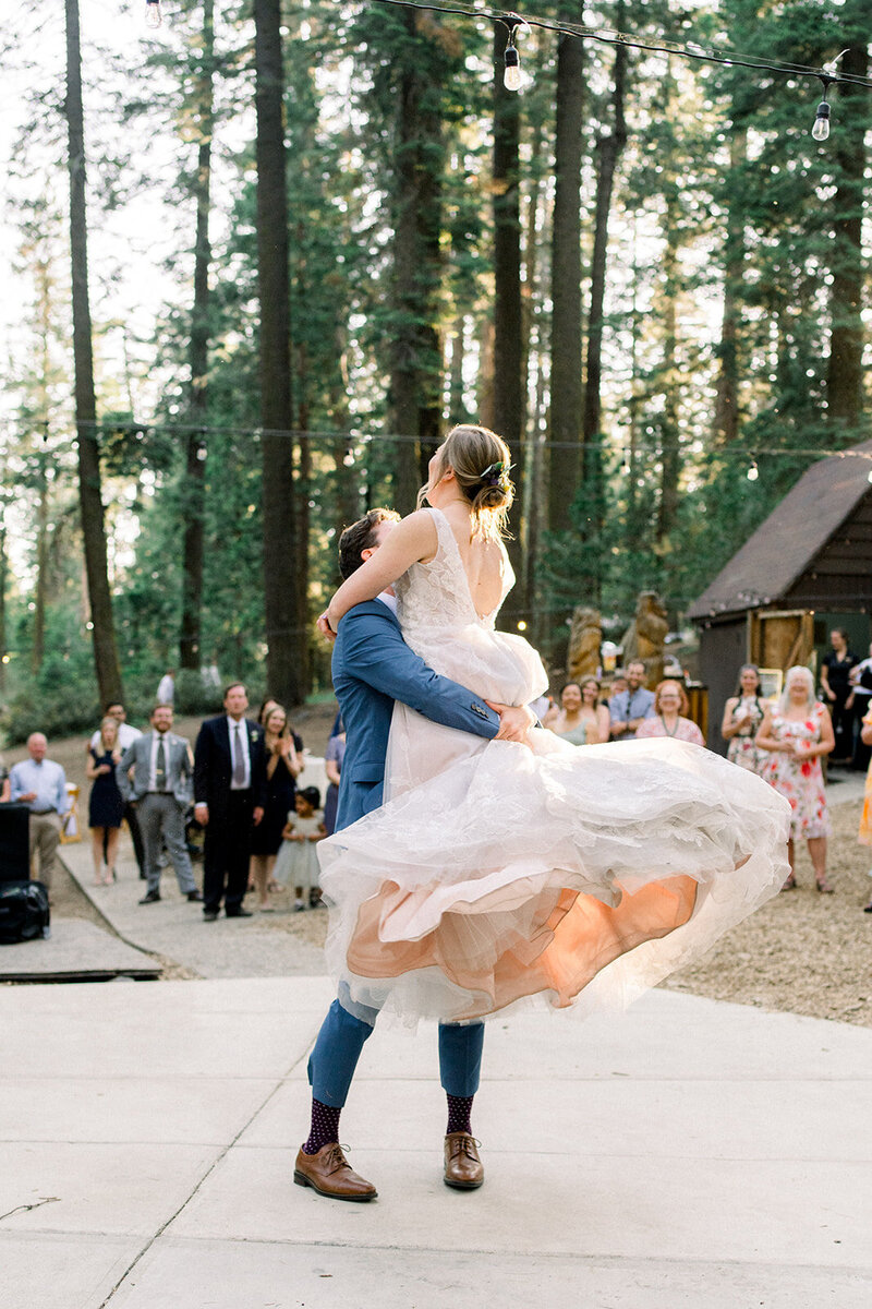 Tiffany Longeway Photography captures a joyous first dance amidst the towering redwoods at Nestldown in Los Gatos, California. The bride and groom’s exuberant celebration, surrounded by nature and twinkling lights, creates a magical atmosphere, perfect for couples seeking a unique and enchanting wedding experience in a luxurious forest setting.