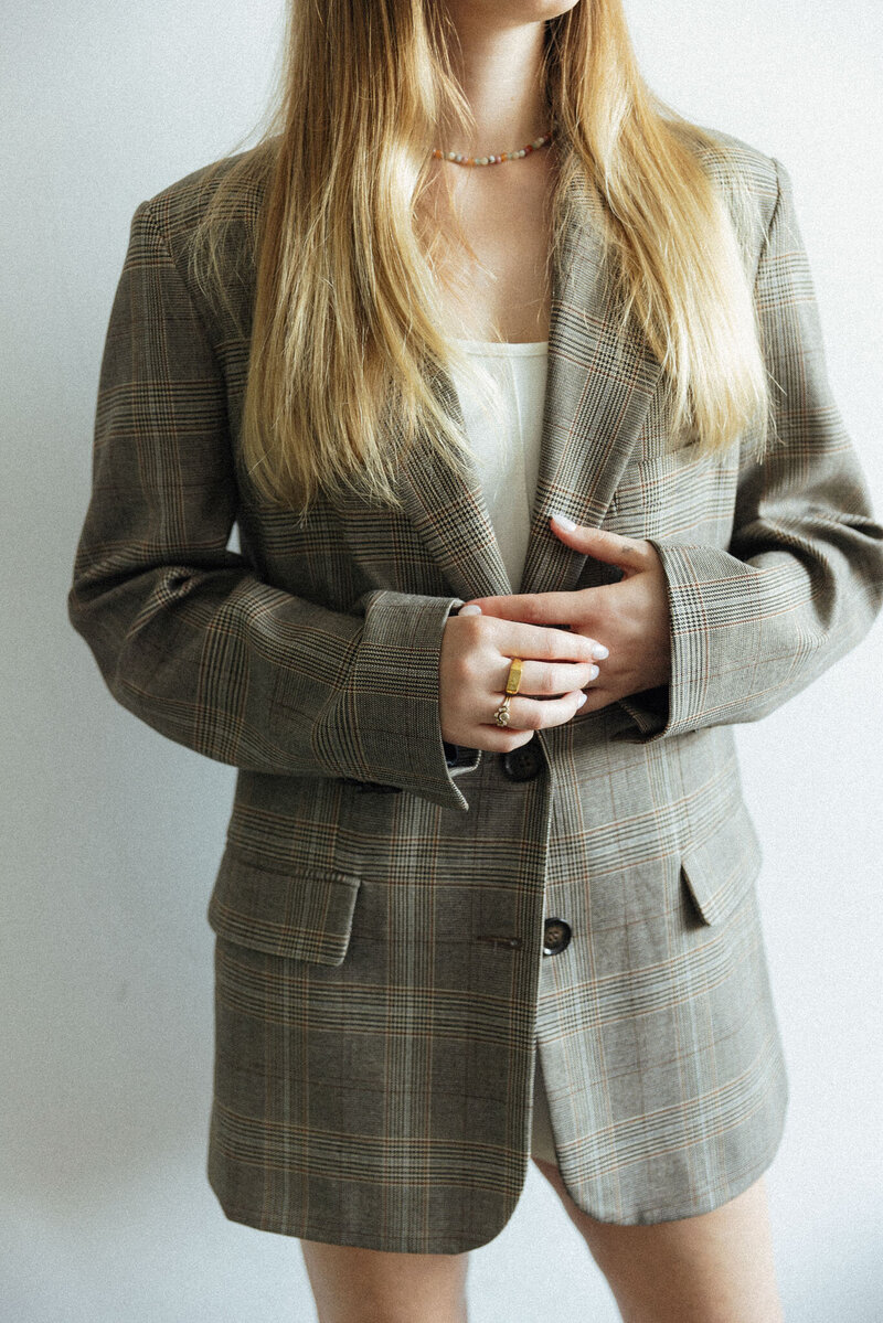 Blazer im Vordergrund, während Hände ihn elegant halten oder präsentieren.