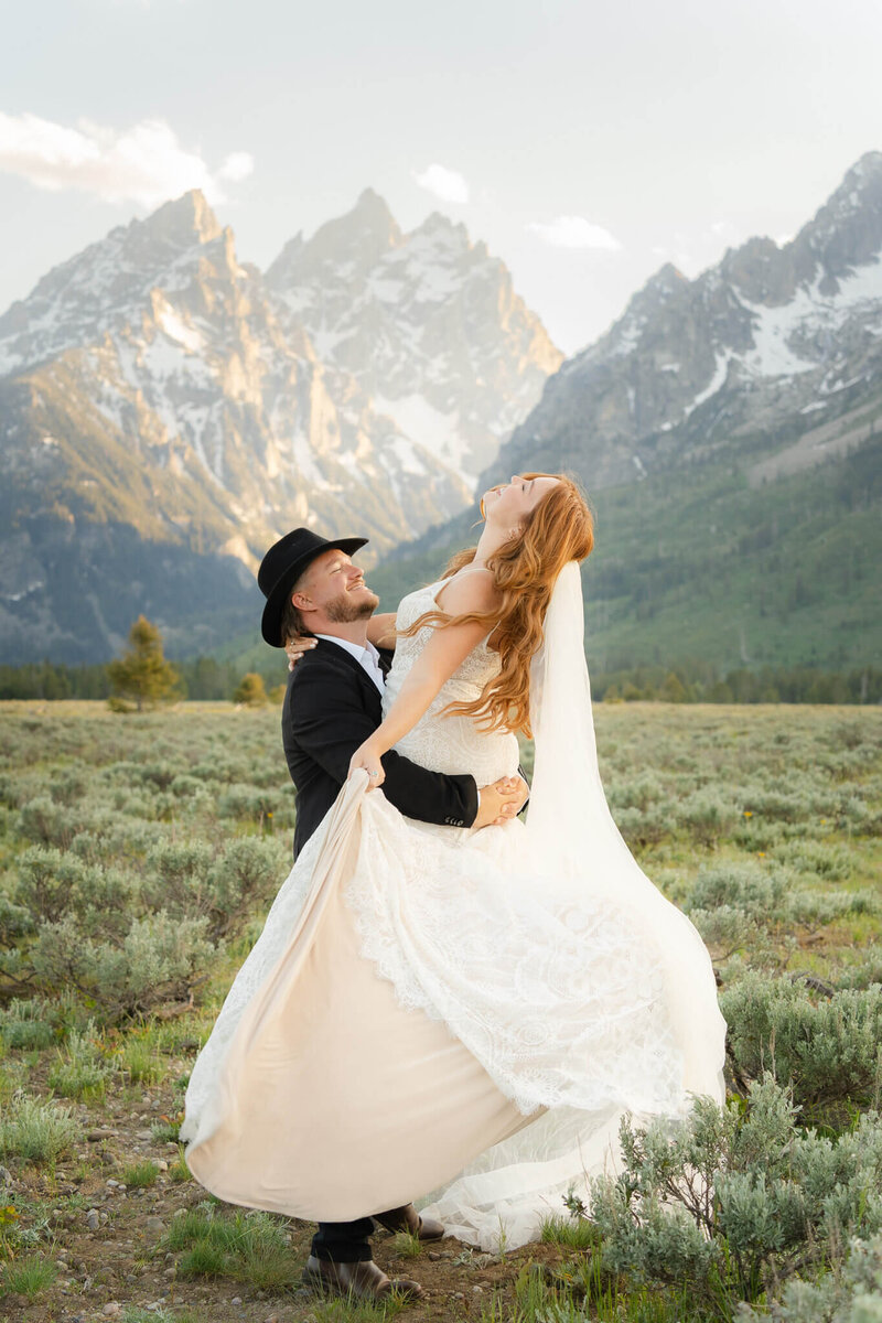 Groom holds his wife and twirls her around with the mountains behind them