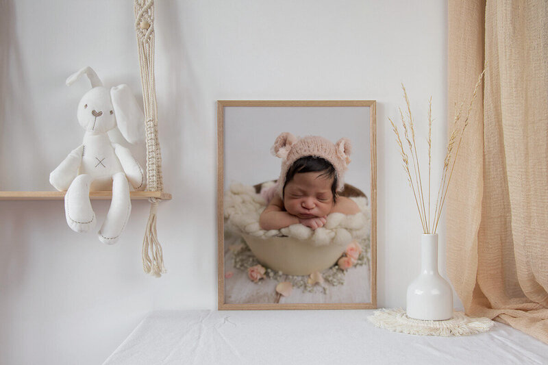 Example of a framed photo in a nursery of a newborn baby girl in a beige bucket and roses at the base
