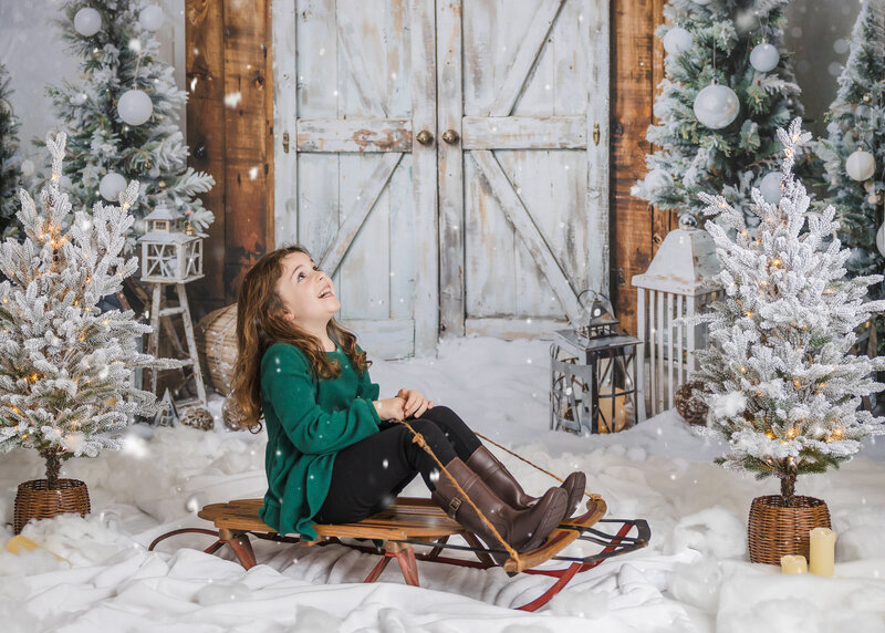 Holiday portrait of girl on sled looking up at snow at Allison Reilly's Union County, NJ photo studio.