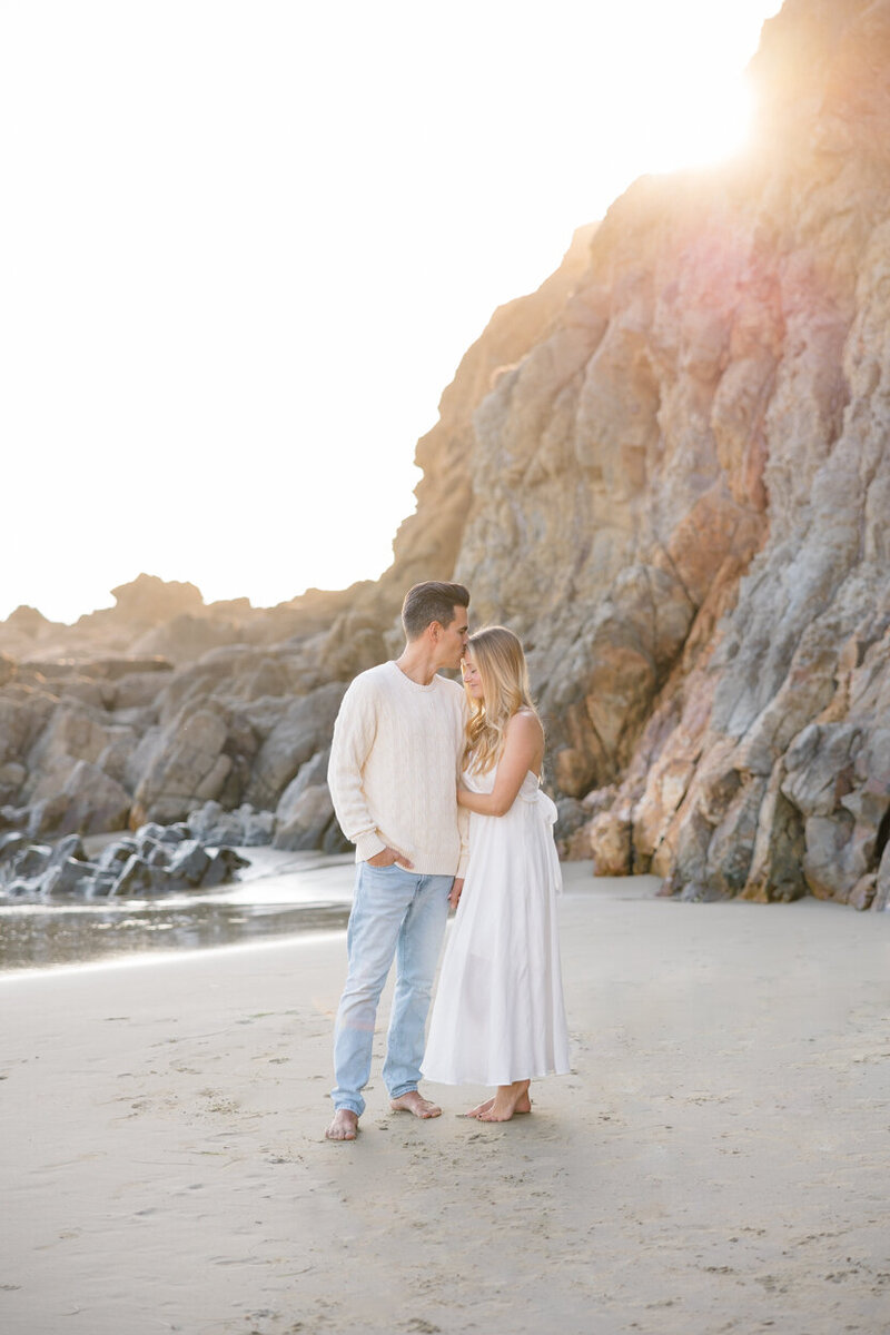 couple on the beach where he is kissing her forehead