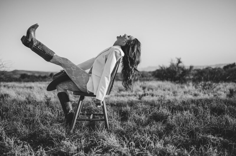 Black and white outdoor brand photo of Juliet Trnka sitting on a chair, posing