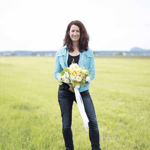 Susan King standing in a field holding a bouquet of flowers