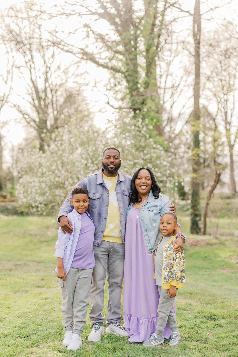 A mom and dad stand in a park with their arms around their young son and daughter for a Ann Arbor Family Photographer