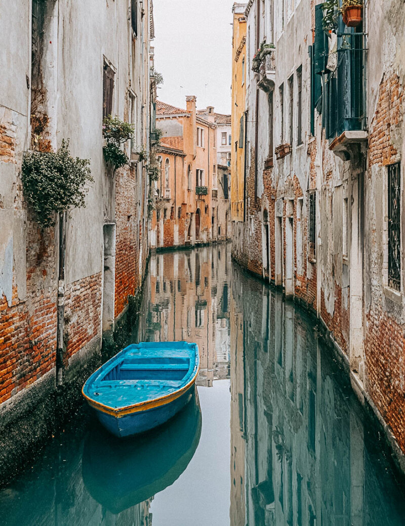 Blue gondola in quiet Venetian waterway symbolizing journey about to begin. Tailored Oasis Travel Co.