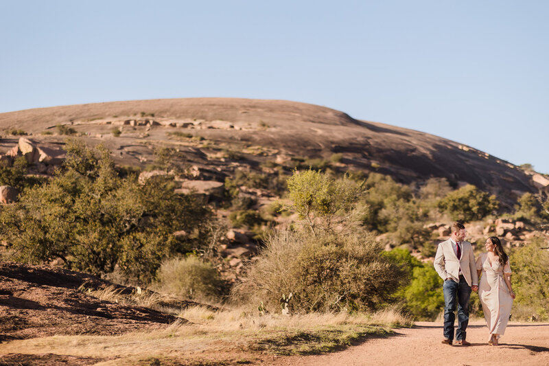 Couple walk along the path during their engagement session at Enchanted Rock in Fredericksburg, Texas. Photo taken by Austin Engagement Photographers, Joanna & Brett Photography