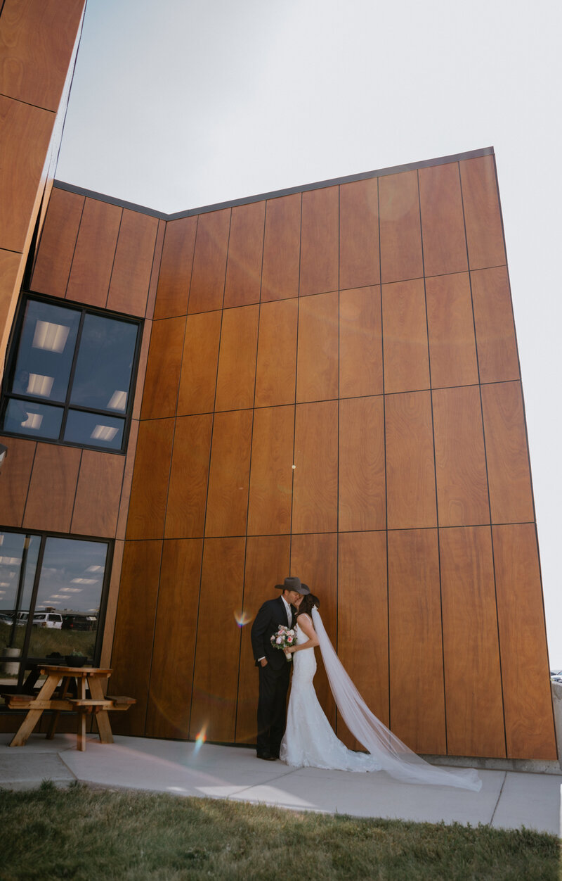 bride and groom kissing in front of big building  taken by fargo wedding photographer kiella lawrence