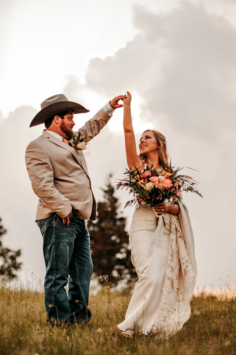 groom twirls his bride as they dance together in a field for their fall wedding day