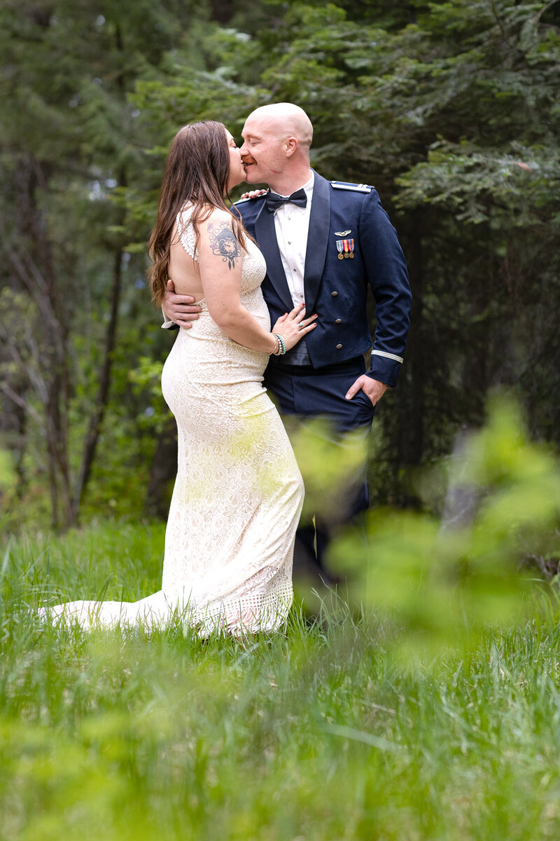 Bride in Dress Groom in military blues facing each other kissing in the forest.