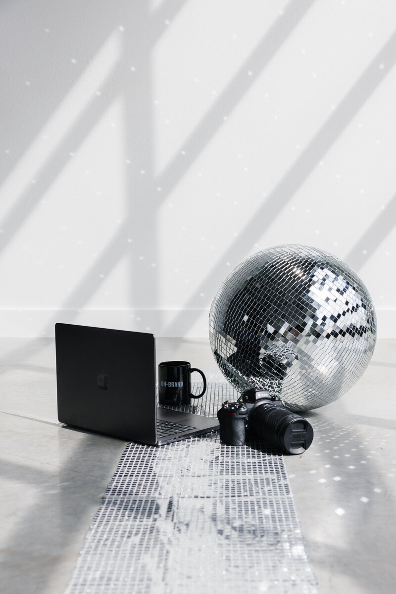 Laptop sitting next to disco ball with coffee cup and camera