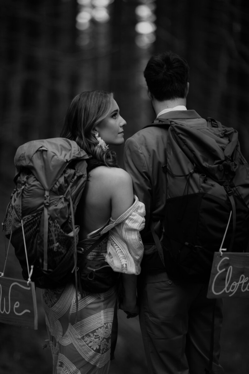 black and white image bride and groom with backpacks
