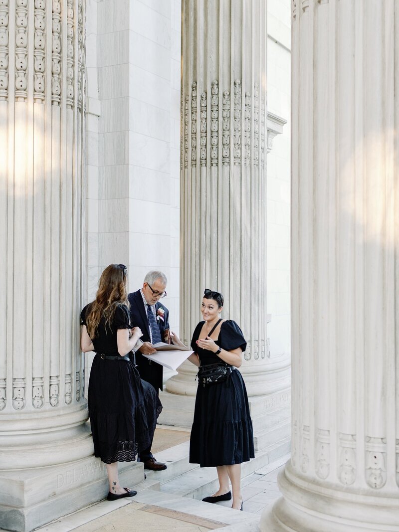 Wedding planners in black dresses discuss details under stone columns of the DAR Constitution Hall