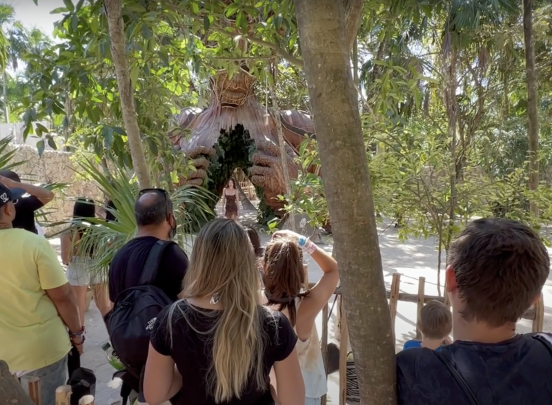 Wooden statue in Tulum covered by visitors, surrounding trees, and cameras