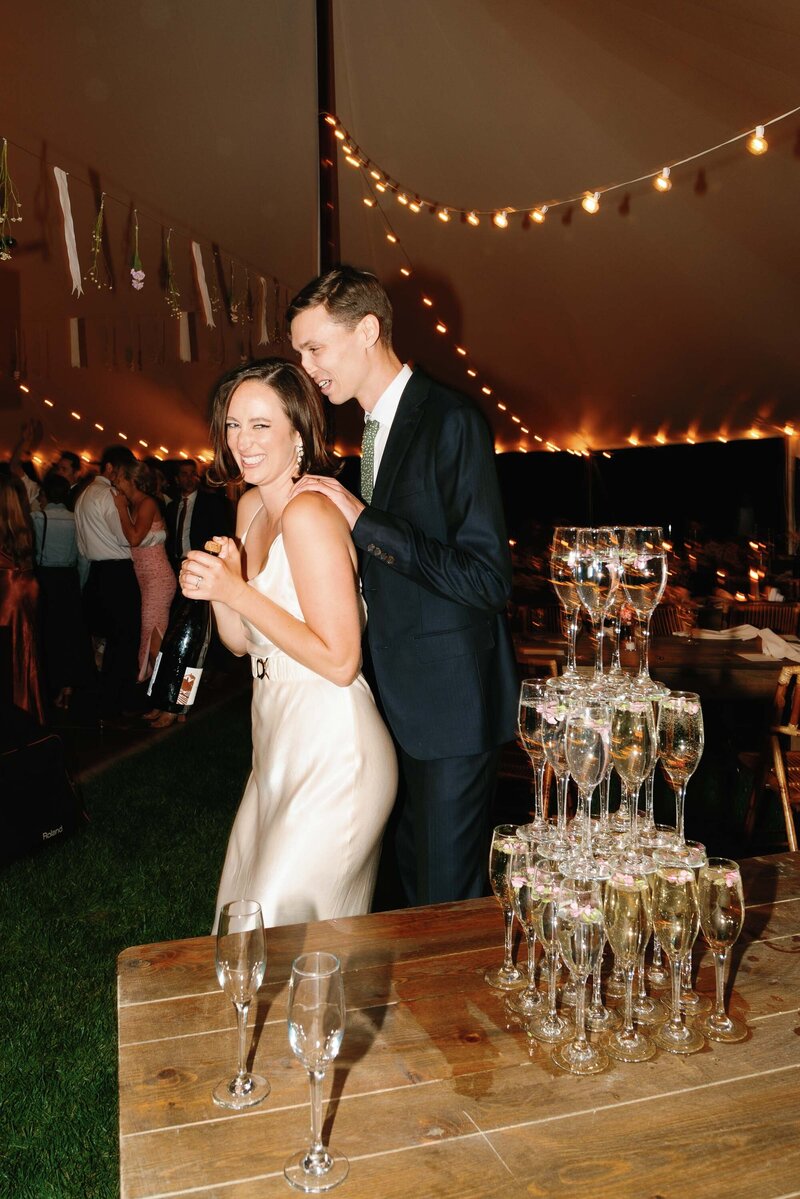 bride pops champagne in silk wedding dress at tented wedding reception by harlow dahlia events