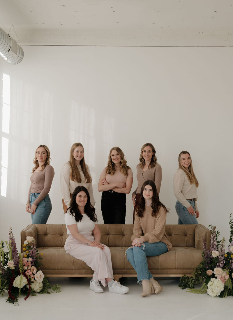 Liz, event planner milwaukee wi / owner of Dream Weddings WI, poses around a couch decorated with florals with her other lead planners and wedding assistants.