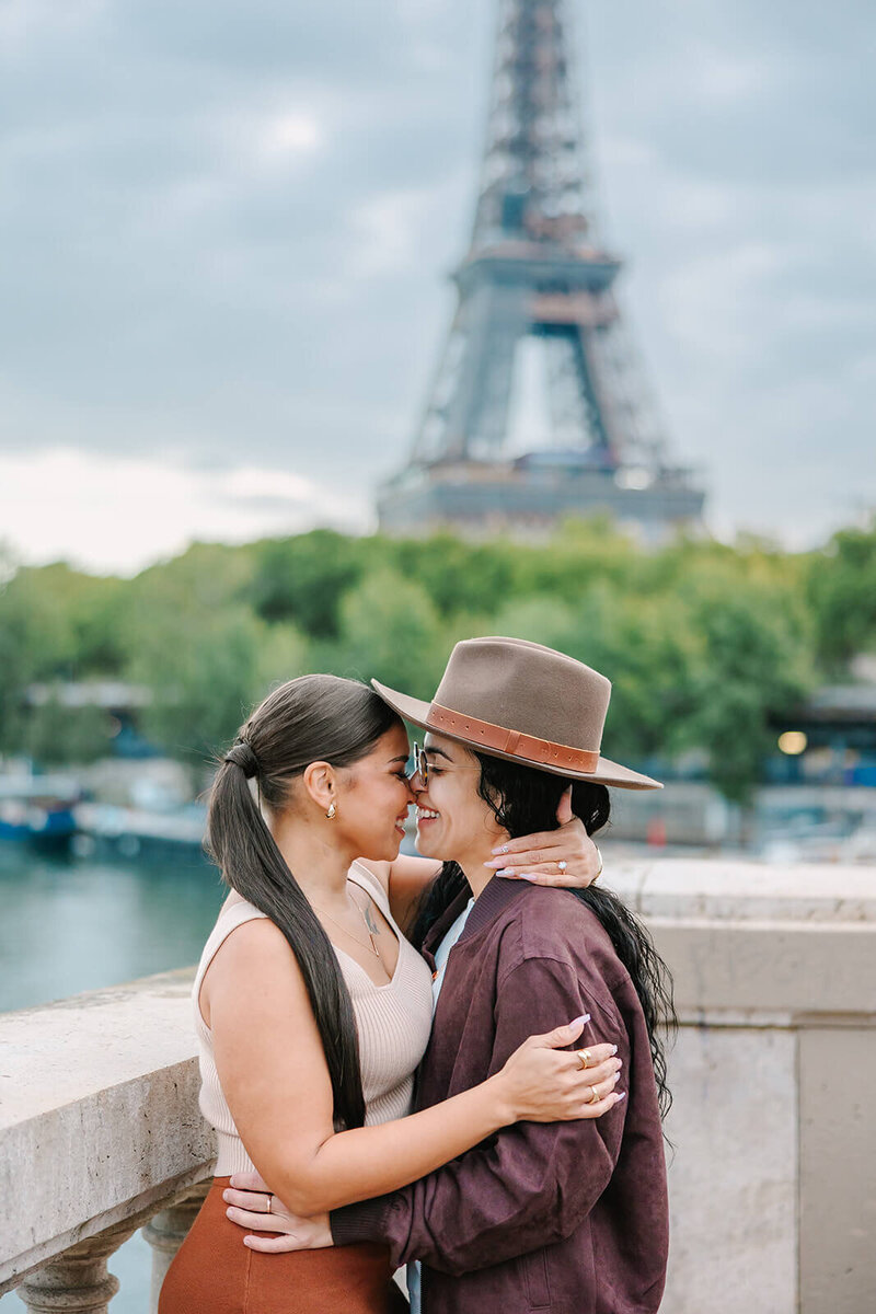 Lesbian couple laughing and kissing after a Paris proposal near the Eiffel Tower at Bir-Hakeim Bridge — captured during a romantic photoshoot by Rachael Laporte.