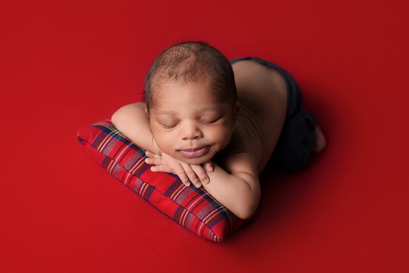 Burnaby newborn photoshoot with smiling baby boy in bright red and blue with chin on hands