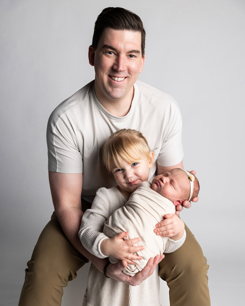 Dad holds newborn daughter with older daughter.
