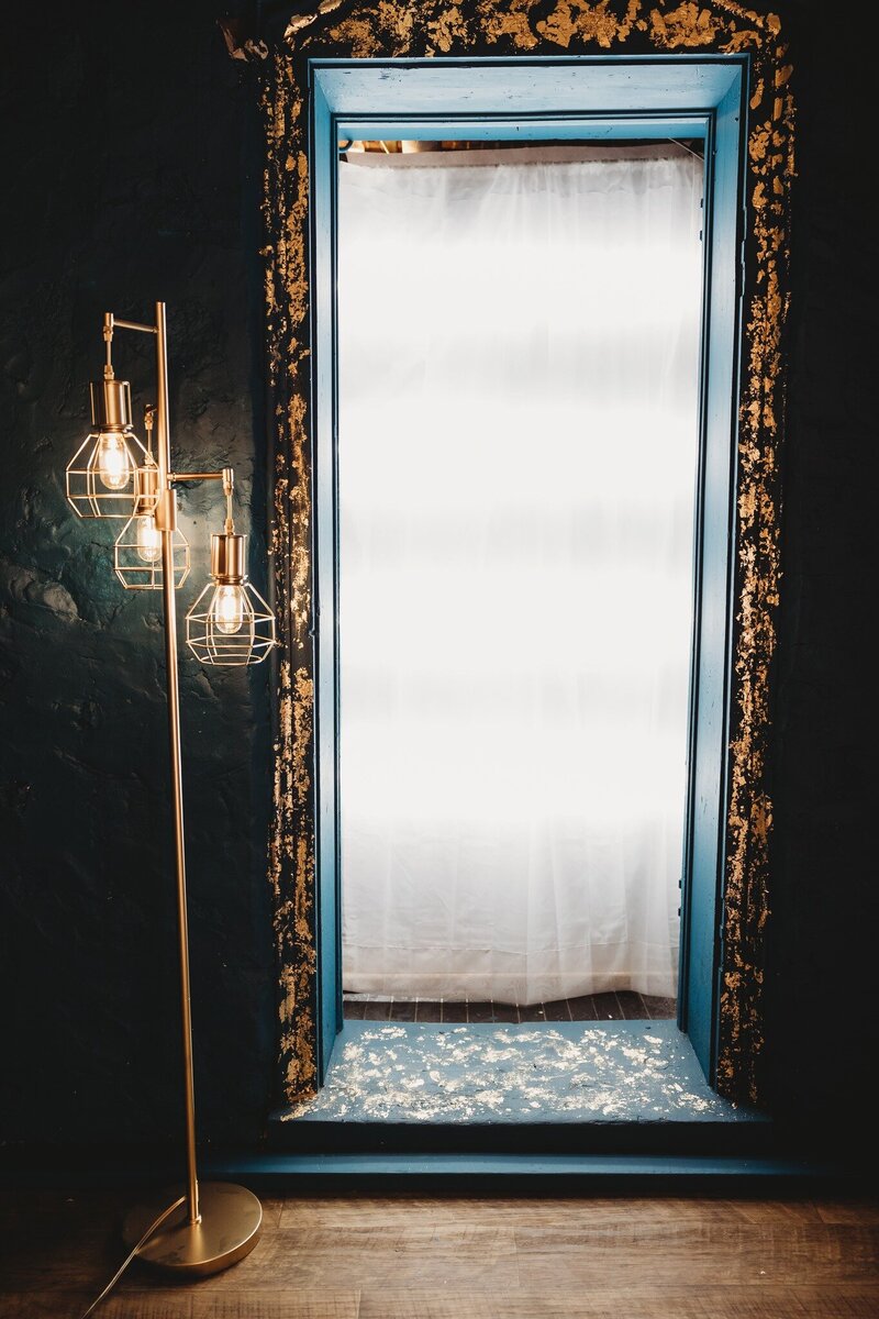 teal doorway with gold leafing and gold lamp