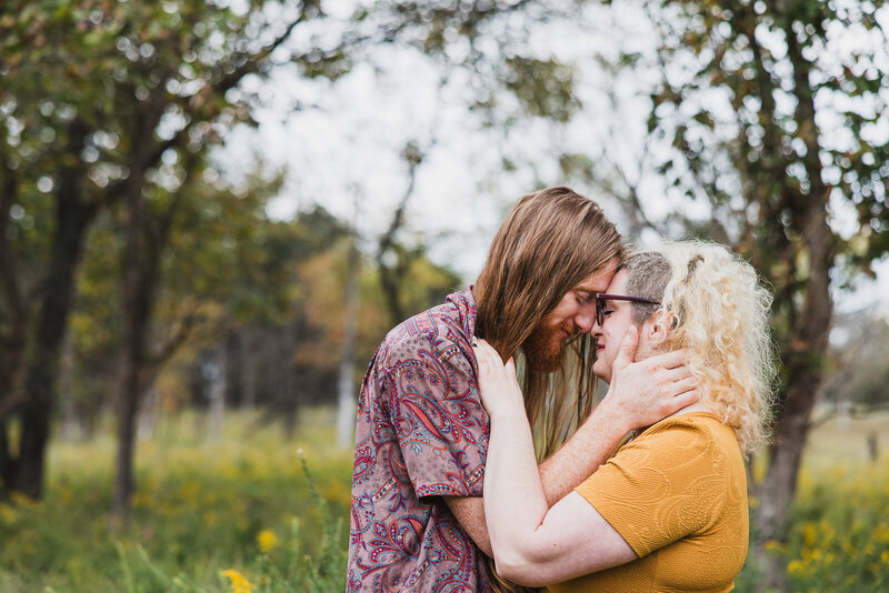 Couple standing in a field of yellow flowers with their foreheads and noses together and holding one another during a portrait session in Bonne Terre, Missouri. 