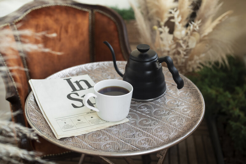 Coffee cup, kettle, and newspaper on a table, creating a calm morning vibe for coaching with Emily