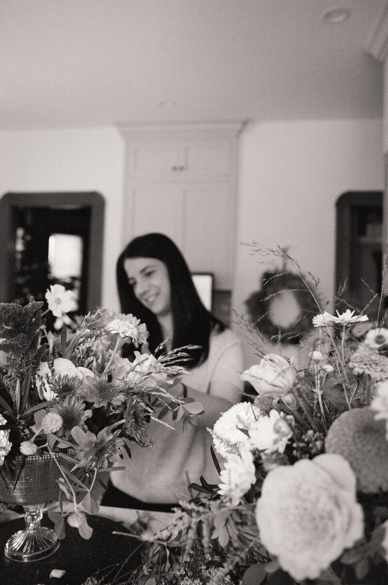 Florist Roxy working on a bouquet in a black-and-white image, surrounded by fresh flowers and focused on arranging stems at her studio work table.