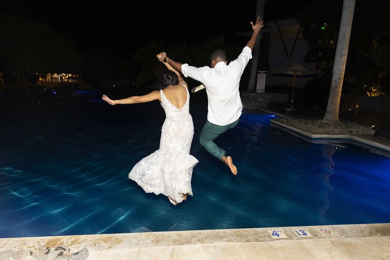 A bride and groom jumping into a pool at night.