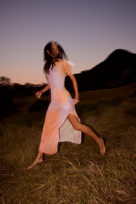Model in colourful dress running through grassy field at dusk
