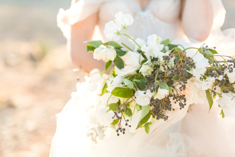  A soft and romantic bridal bouquet with white garden roses, delicate blooms, and trailing greenery, bathed in desert golden sunlight